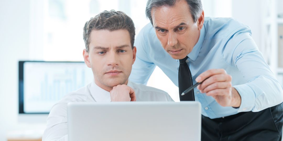 Two business men in suits looking at process efficiency on a laptop together,